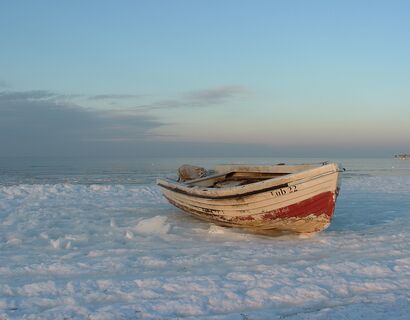 Rot-weißes Boot liegt am mit Schnee bedeckten Strand