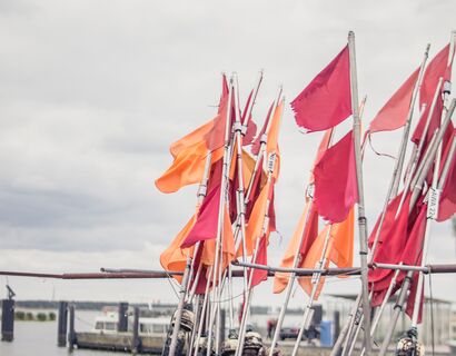rote und orangene Fahnen, dahinter unscharf der Hafen von Altwarp