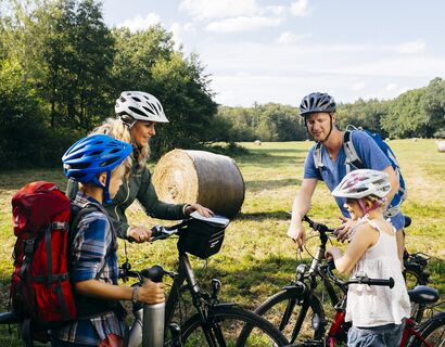 Eine Familie steht mit ihren Fahrräder am Rand eines Feldes und berät sich.