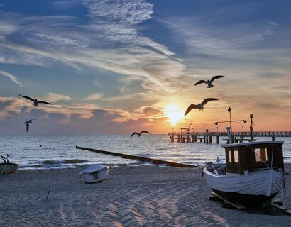 Strand von Koserow in der Abendsonne. Am Himmel fliegen 5 Möwen, im Sand liegen drei kleine Boote.