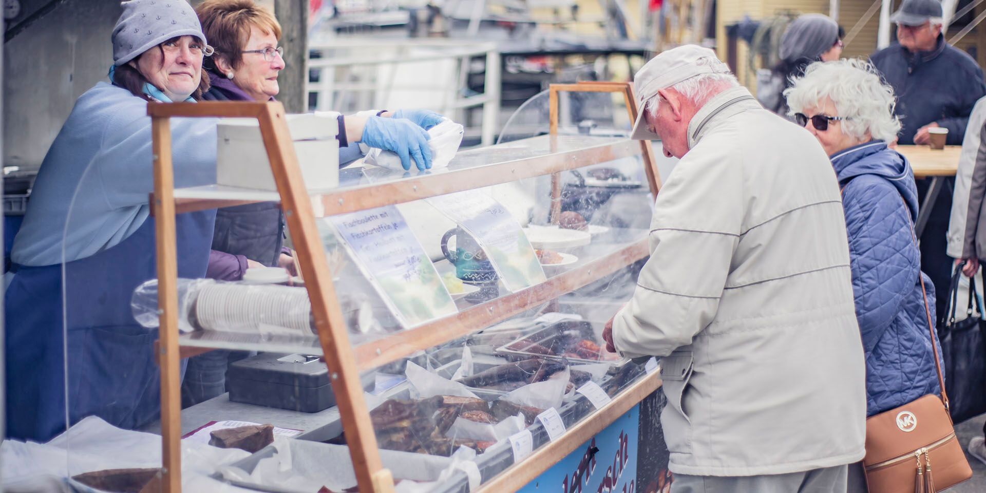 Ein älteres Paar an einem Fischstand, hinter dem zwei Dame stehen.
