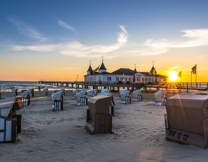Blick auf den Strand im Seebad Ahlbeck bei Sonnenaufgang. Im Hintergrund ist die Seebrücke, im Vordergrund stehen viele Strandkörbe