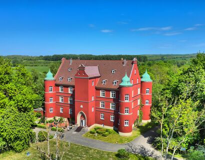 Ein rotes Schloss ist umringt von Bäumen.