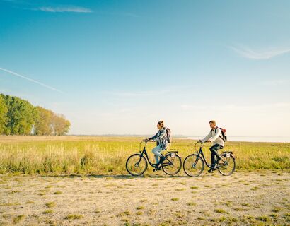 Zwei Radfahrer, ein Mann und eine Frau, fahren hintereinander einen Feldweg entlang