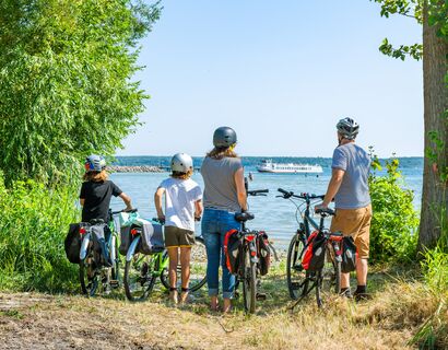 Eine Familie mit Eltern und zwei Kindern steht mit ihren Fahrrädern am Ufer der Müritz und blickt aufs Wasser